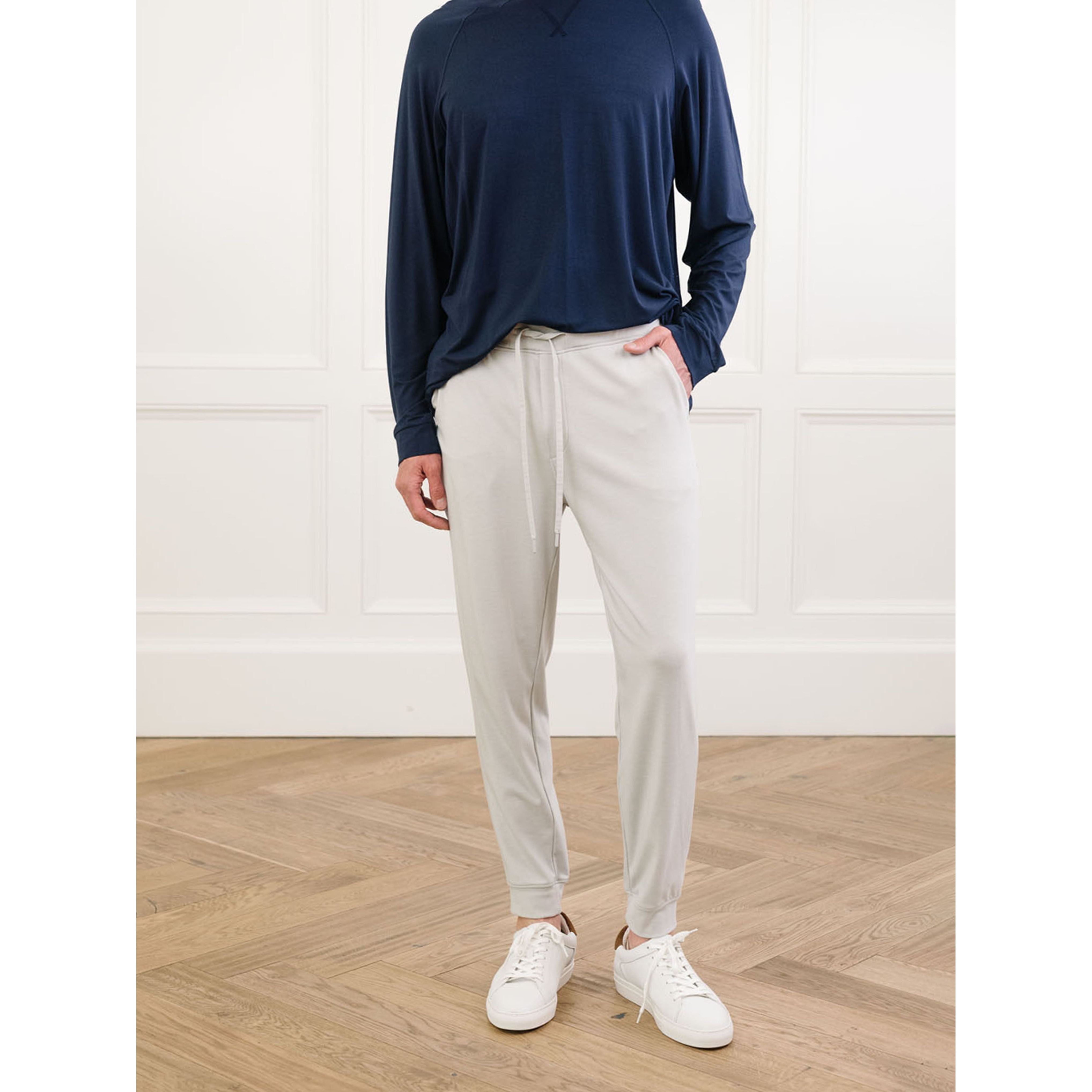 Person wearing a navy long-sleeve shirt, beige pants, and white sneakers in a minimalistic setting.
