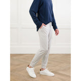 Person wearing a navy long-sleeve shirt, light gray pants, and white sneakers in a minimalistic setting.