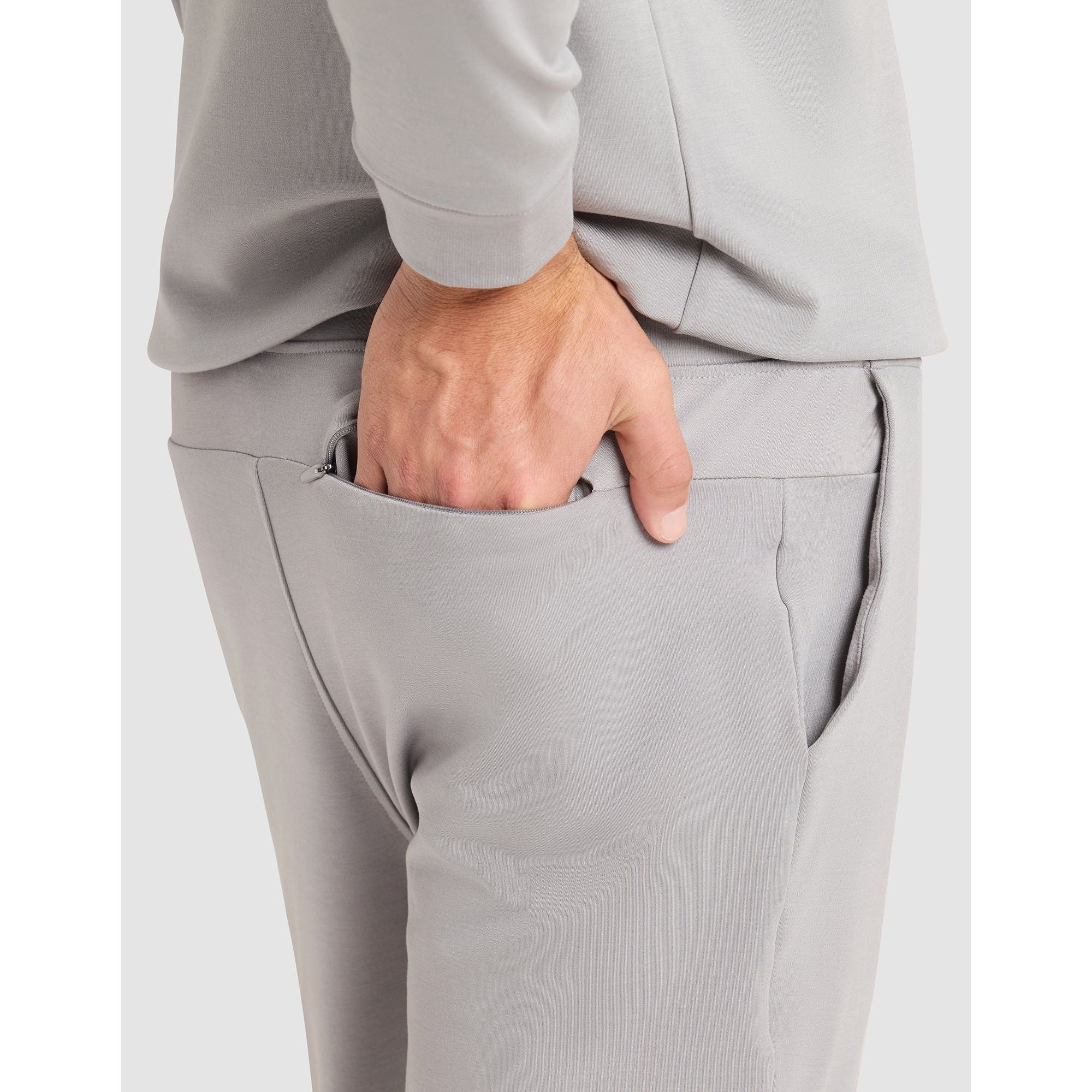 Person wearing gray pants with a hand in one of the pockets on a light gray background