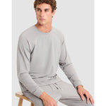 Man wearing a gray tracksuit sitting on a stool against a white background