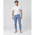 A man wearing a white crew-neck t-shirt and light blue silkcut thermal leggings for men, standing barefoot against a light gray studio background.