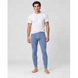 A man wearing a white crew-neck t-shirt and light blue silkcut thermal leggings for men, standing barefoot against a light gray studio background.