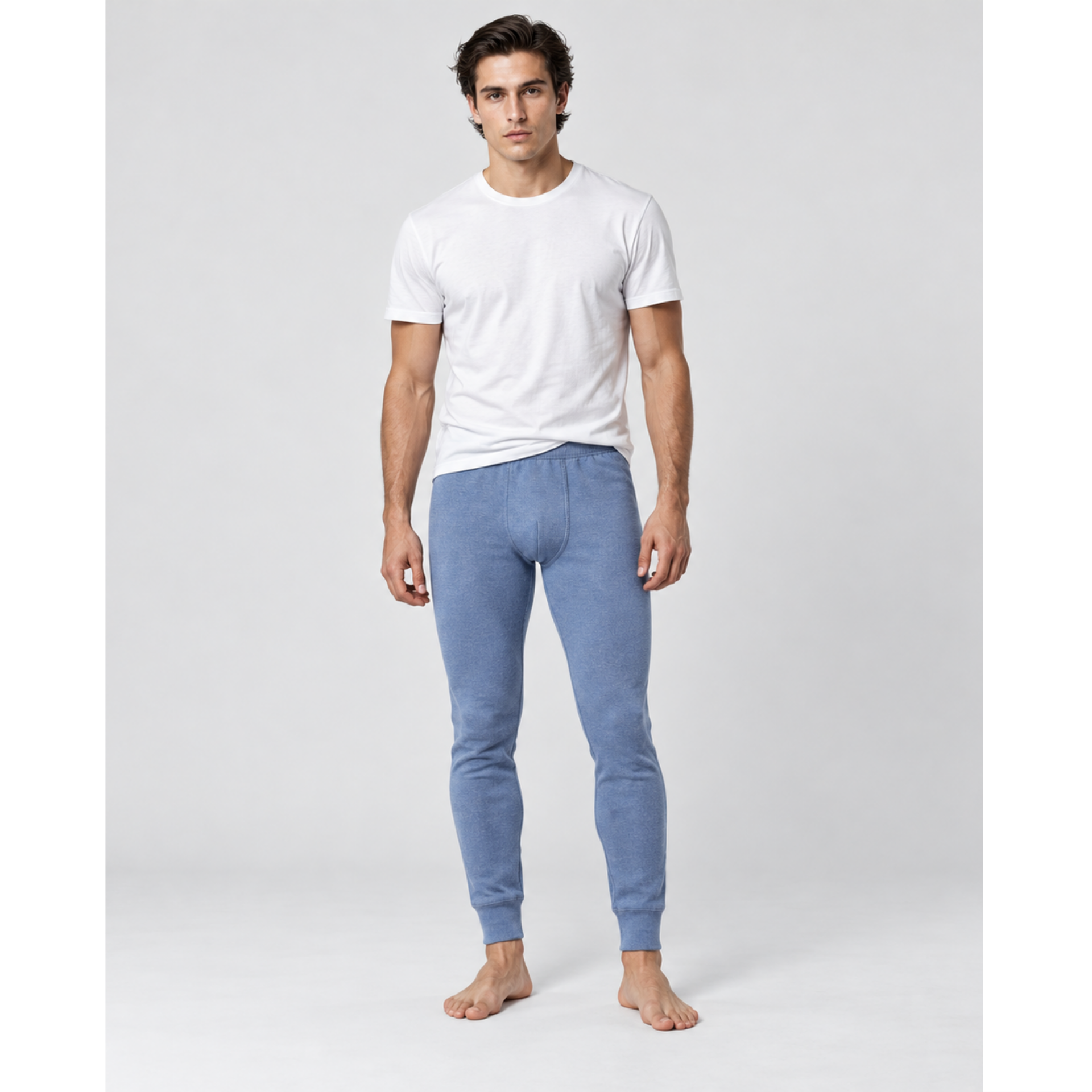 A man wearing a white crew-neck t-shirt and light blue silkcut thermal leggings for men, standing barefoot against a light gray studio background.