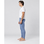 A man in profile wearing a white short-sleeve t-shirt and light blue silkcut thermal leggings for men standing barefoot against a light gray studio background.