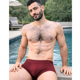 Man wearing maroon underwear by a pool
