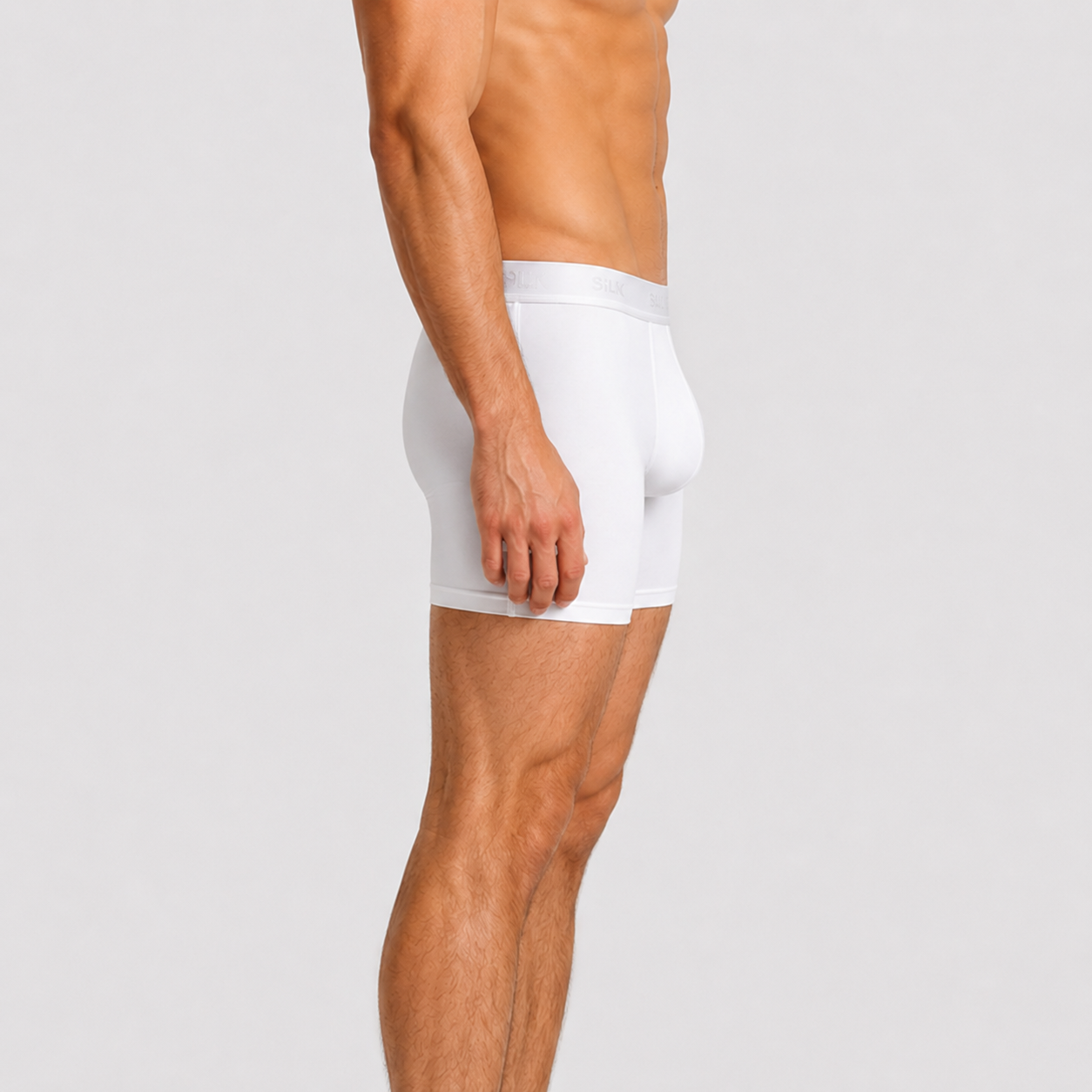 A side-profile view of a male model wearing SilkCut Underwear white boxer briefs against a light gray studio background.